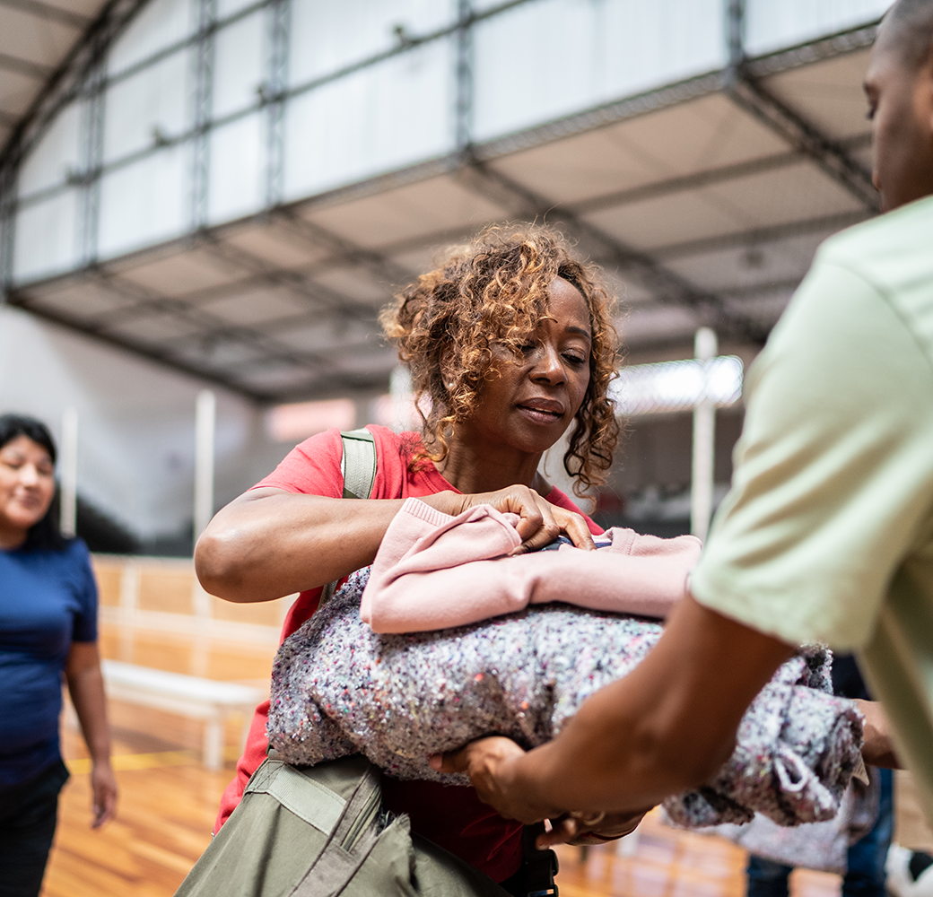 Black woman being handed a blanket by a solider in a gymnasium.