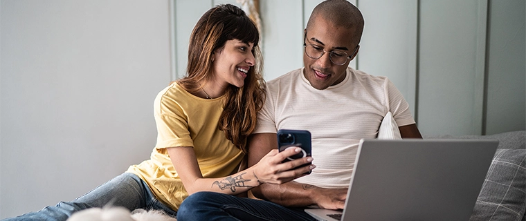 Couple looking at phone and computer with dog next to them